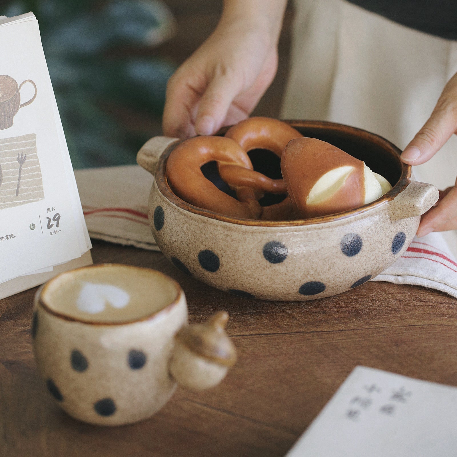Person holding a bowl with pretzels next to a polka dot mug on a wooden table.