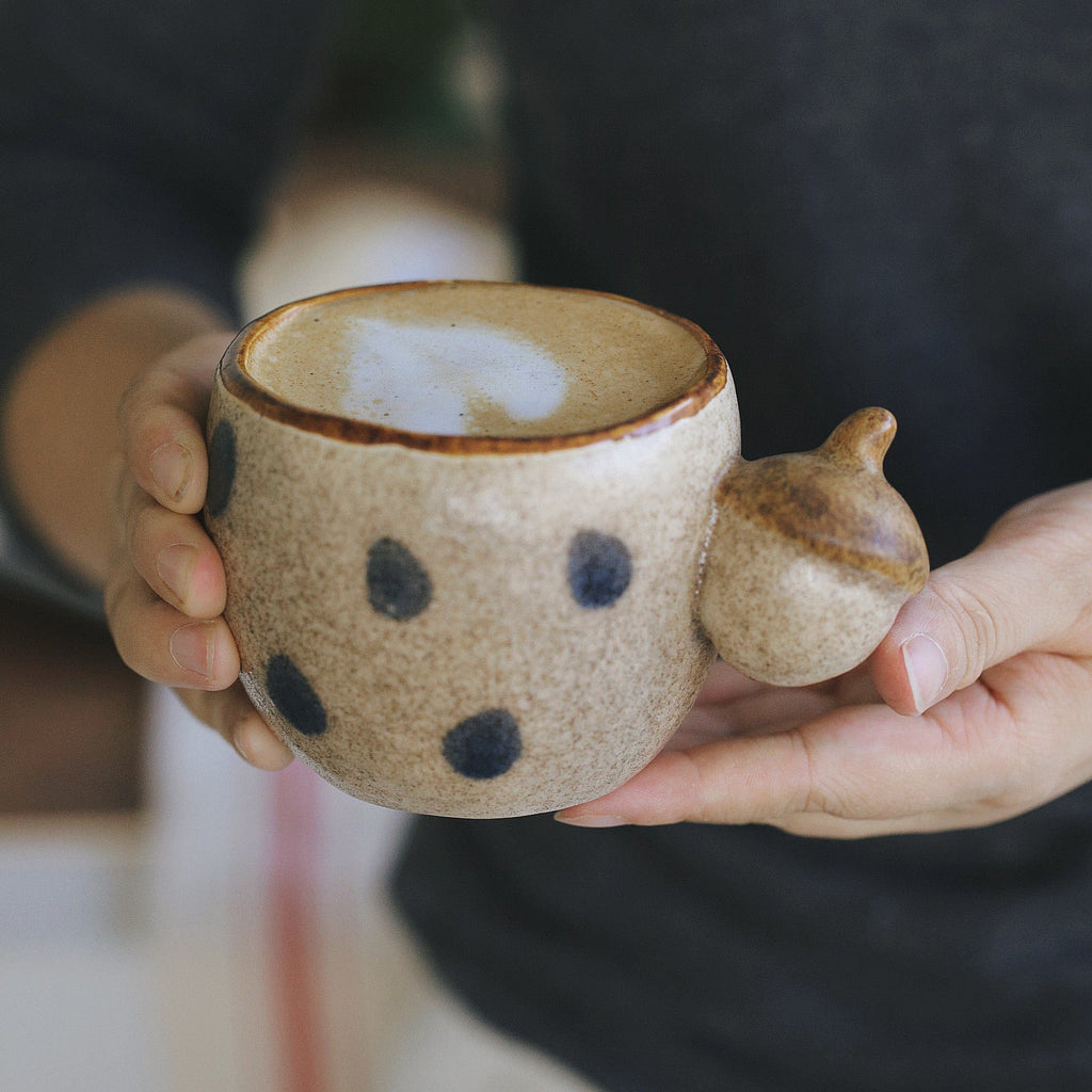 Person holding a ceramic cup with a unique design, blurred background
