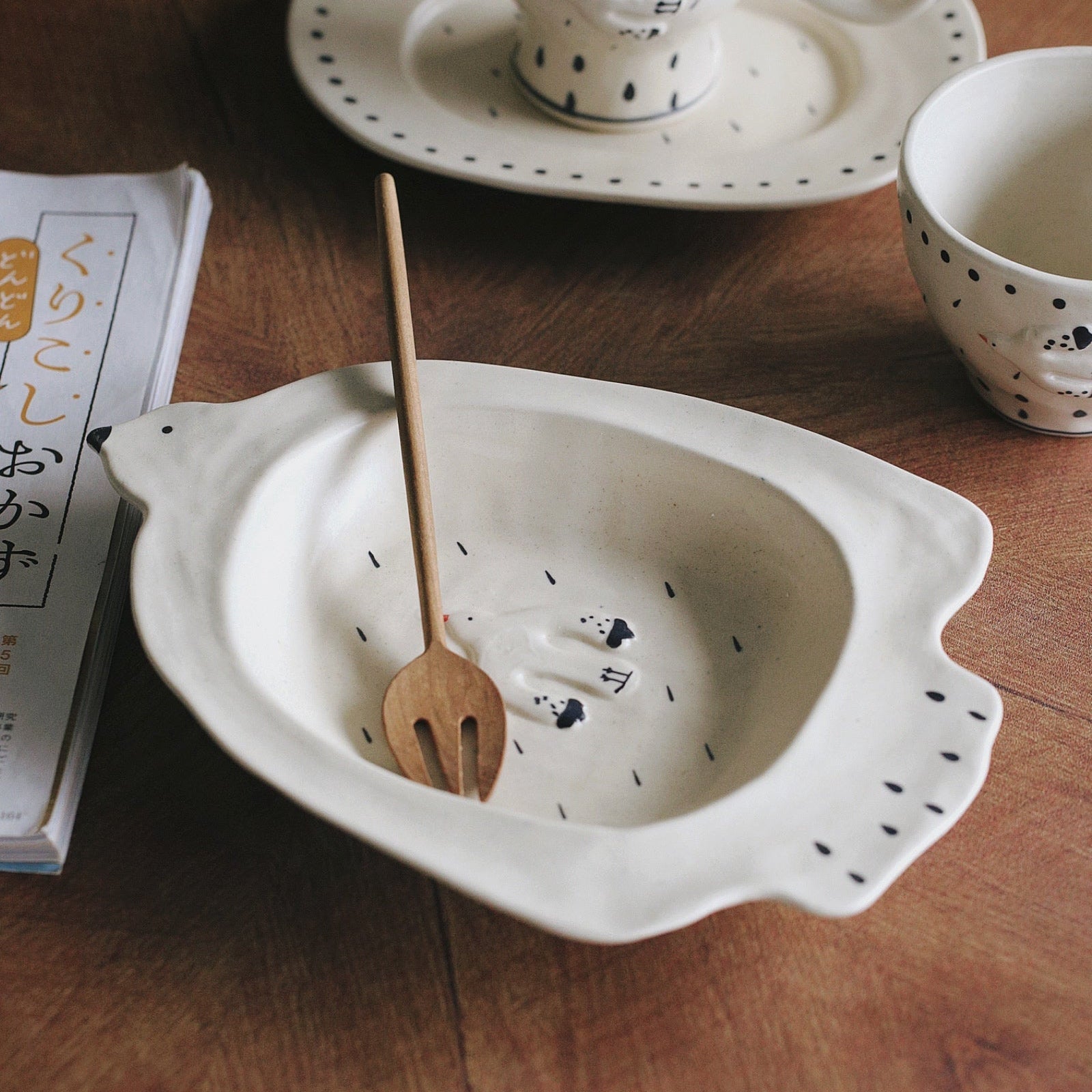 Ceramic bowl with a wooden spoon, cup, and saucer on a wooden table.
