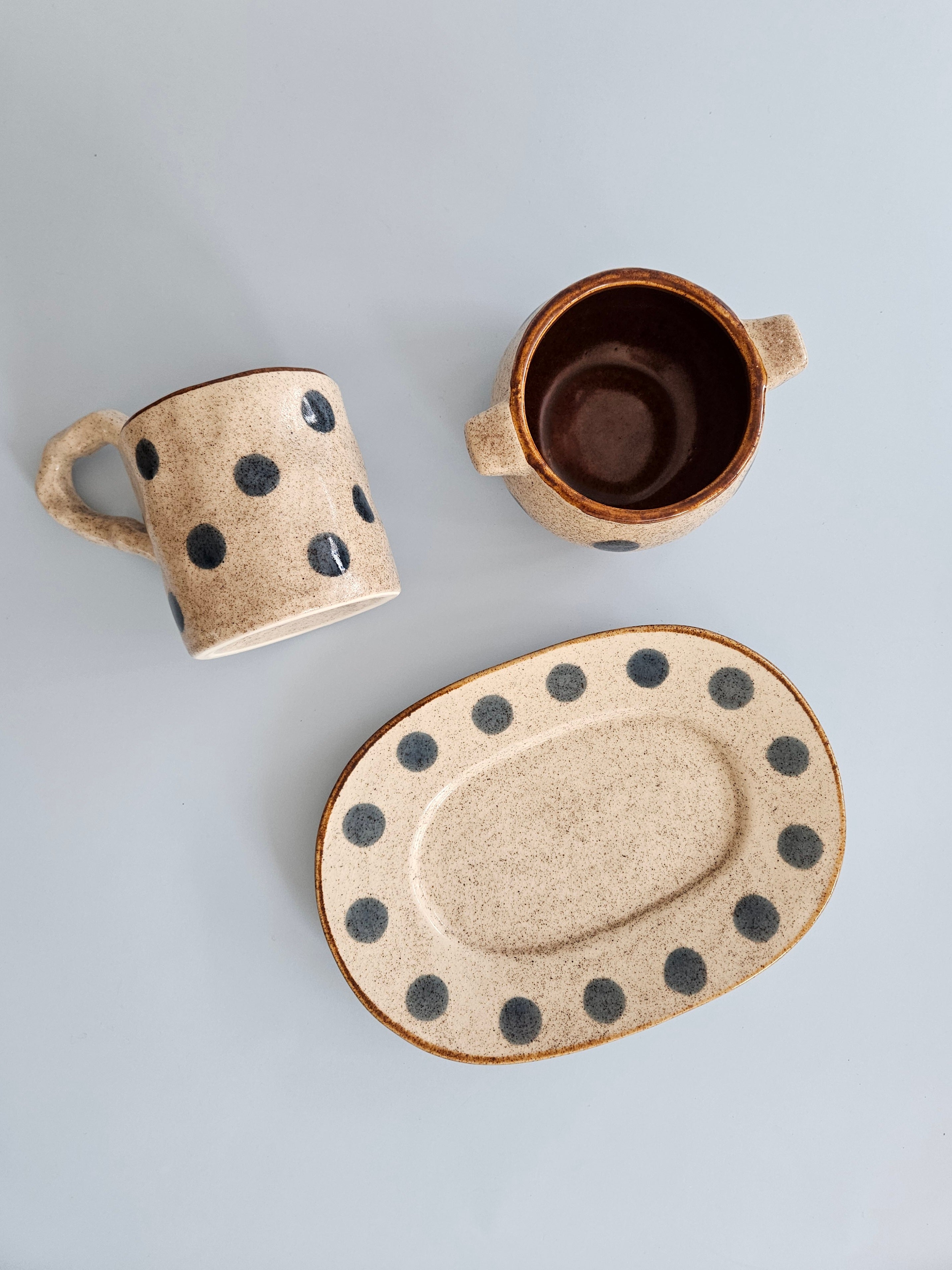 Set of ceramic mugs and a plate with black dot patterns on a light gray background