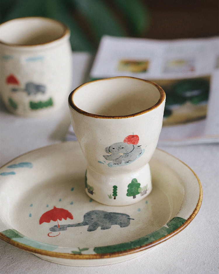 Ceramic cup and saucer with animal illustrations on a light surface.