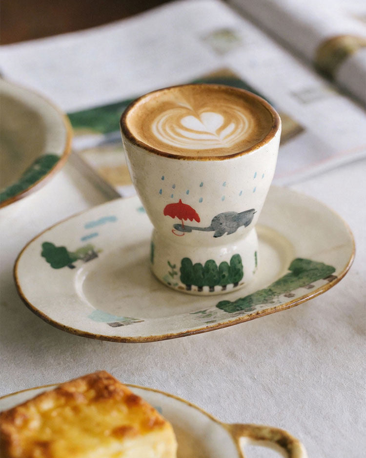 Cappuccino in a decorative cup with a heart design on a saucer, accompanied by a pastry on a table.