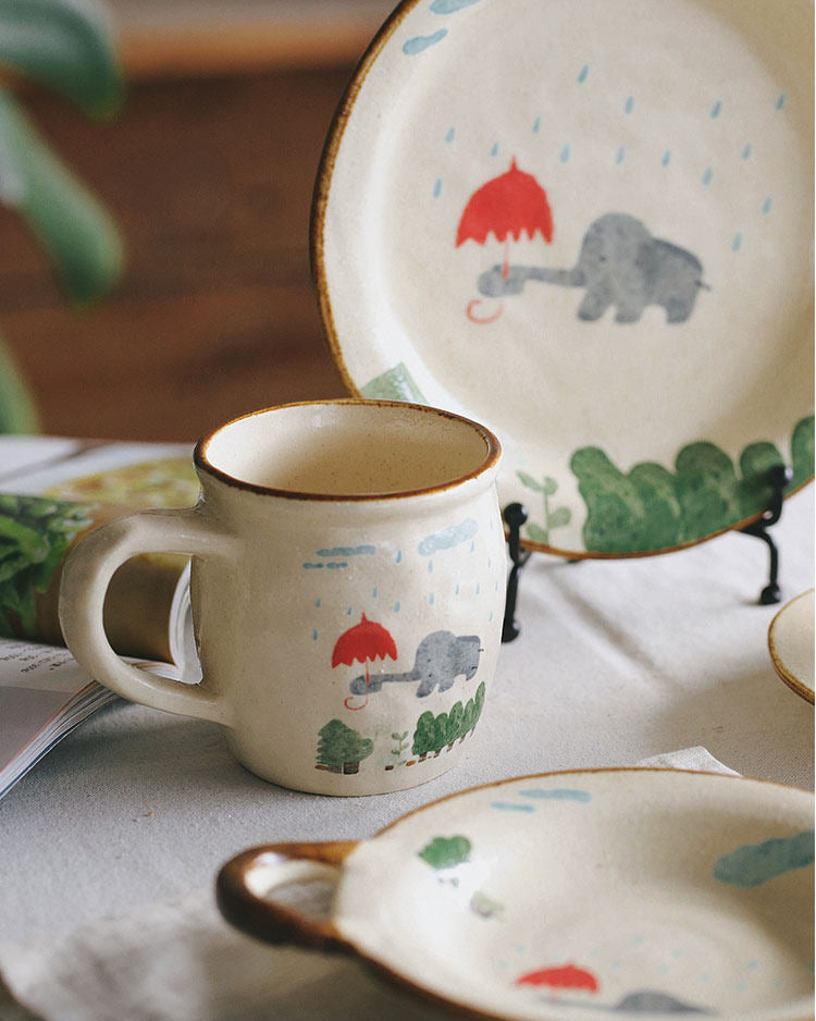 Ceramic mug and plates with animal illustrations on a table.