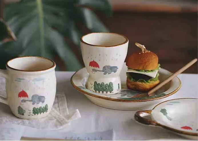 Ceramic cups and bowls with animal illustrations on a white tablecloth.
