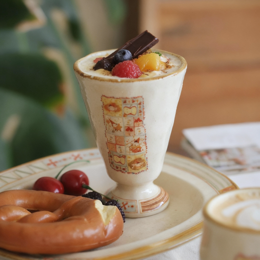 Decorative dessert cup with fruit toppings on a table with a donut and coffee.