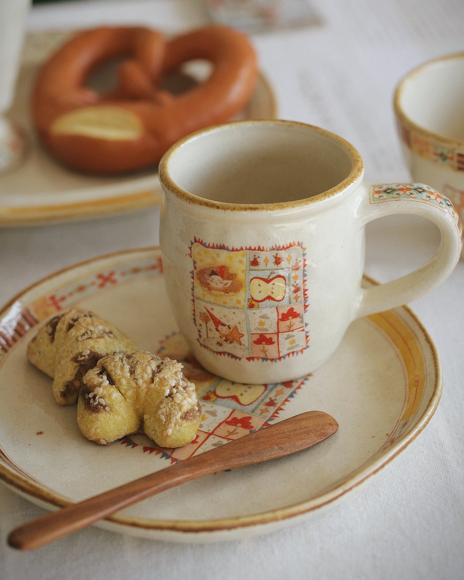 Cup with decorative pattern on a plate with cookies and a pretzel on a table.