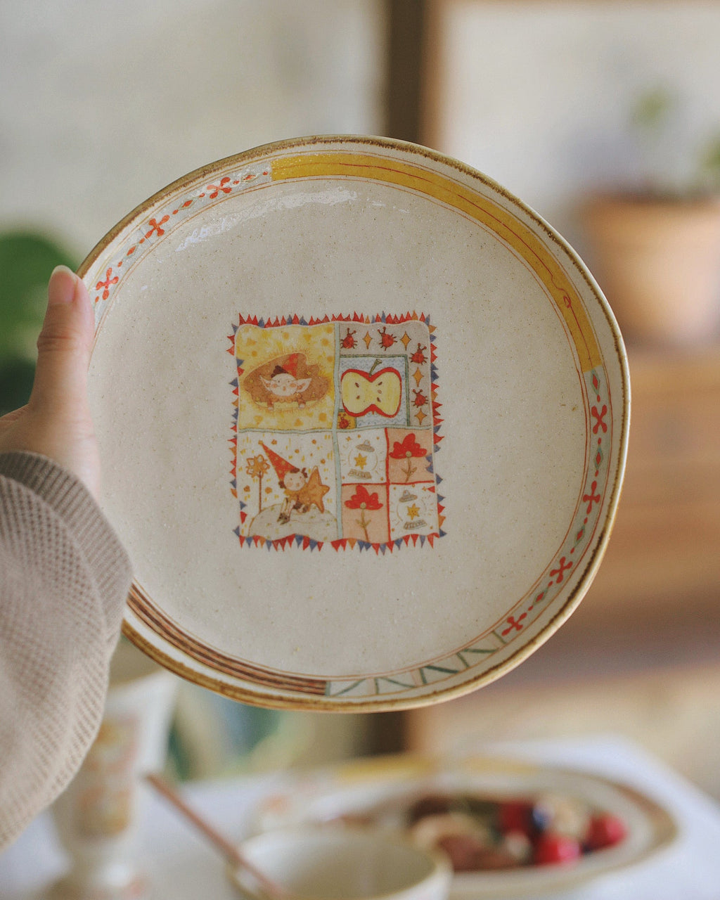 Decorative plate with a colorful design held by a hand, blurred background of a table setting.