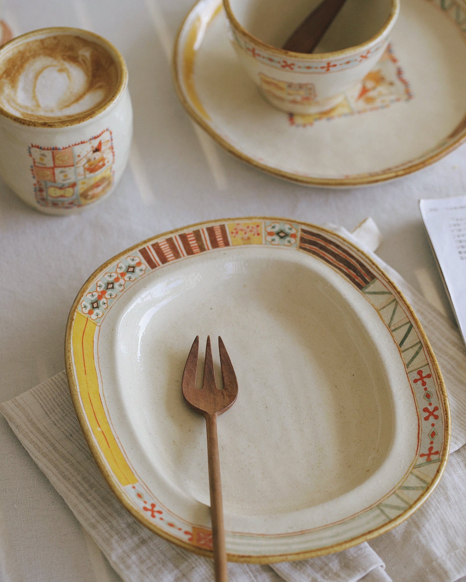 Café setting with a plate, fork, and cups on a white tablecloth.