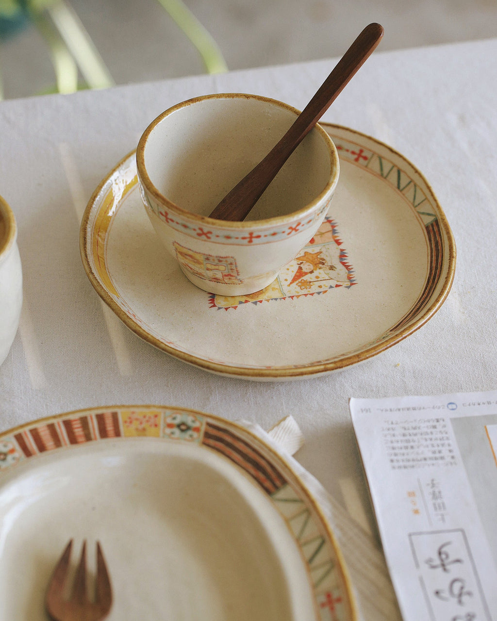 Cup with saucer and spoon on a table with a fork and paper.