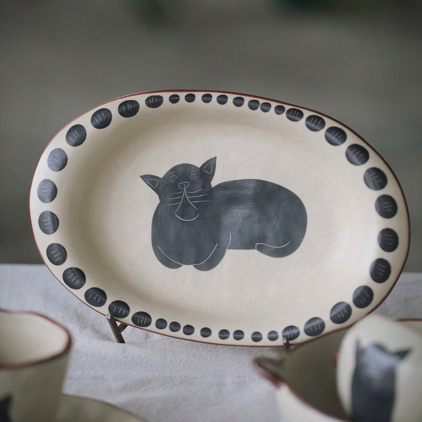 Ceramic plate with a black cat design on a table with other ceramic items.