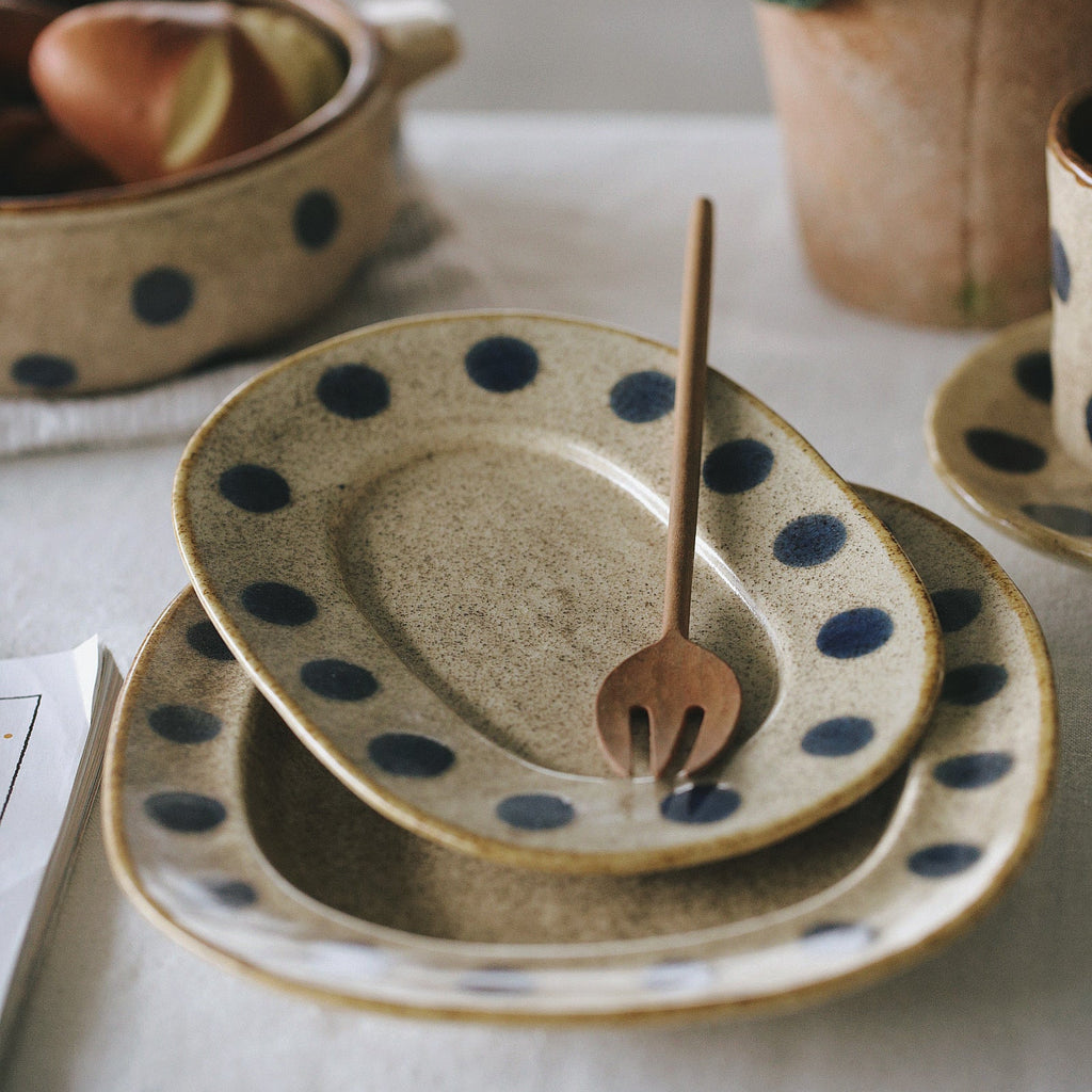 Set of ceramic plates with blue polka dots on a table with a plant and bowl in the background.