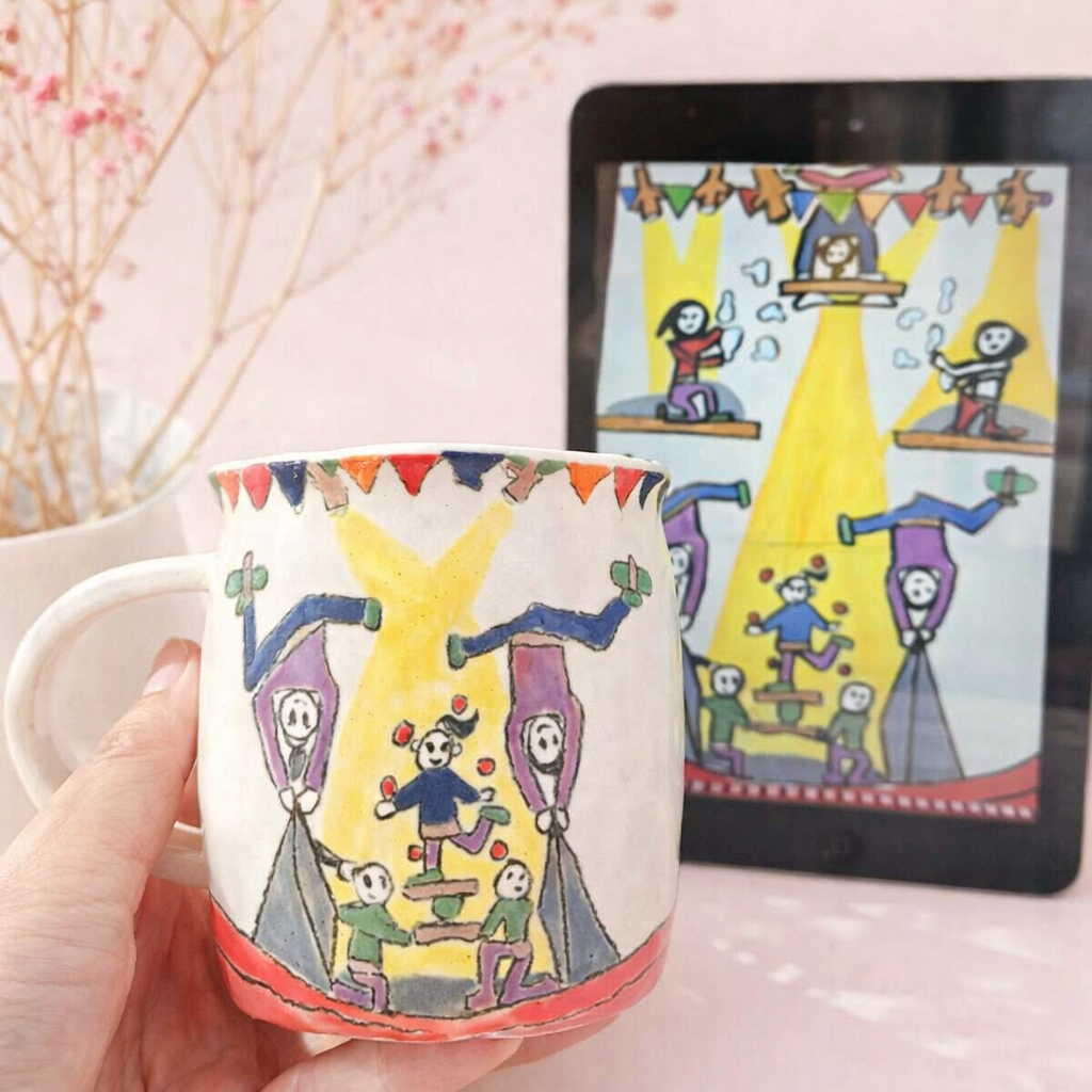 Mug with artistic design of people on a stage held by a hand, with a tablet displaying the same design in the background.