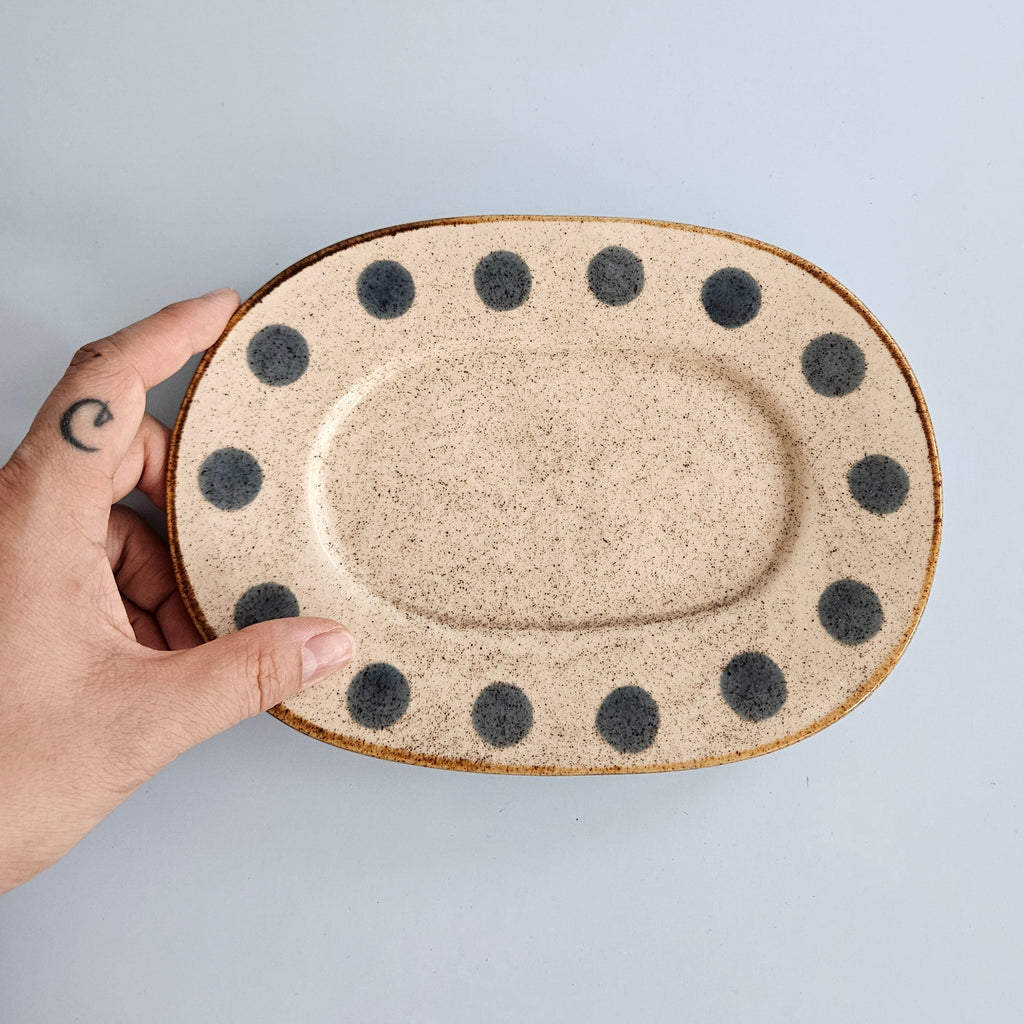 Hand holding a ceramic plate with black dot patterns on a light gray background