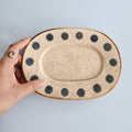 Hand holding a ceramic plate with black dot patterns on a light gray background