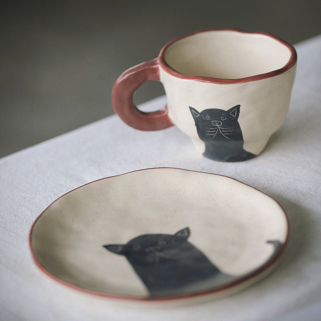 Ceramic mug and plate with cat illustrations on a neutral background