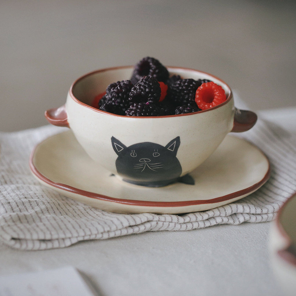 Ceramic bowl with cat design filled with berries on a white surface