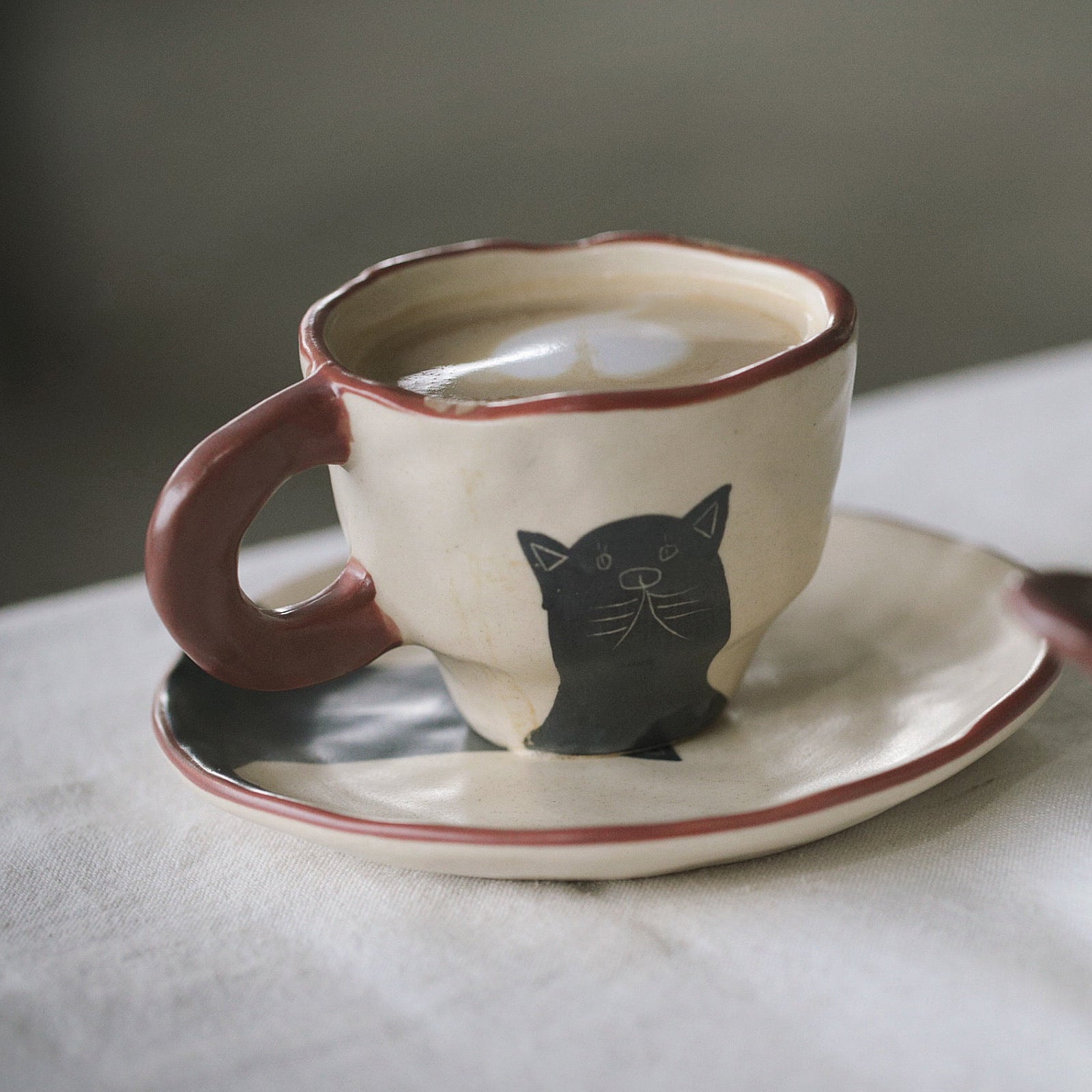 Ceramic cup and saucer with a cat design on a marble surface.
