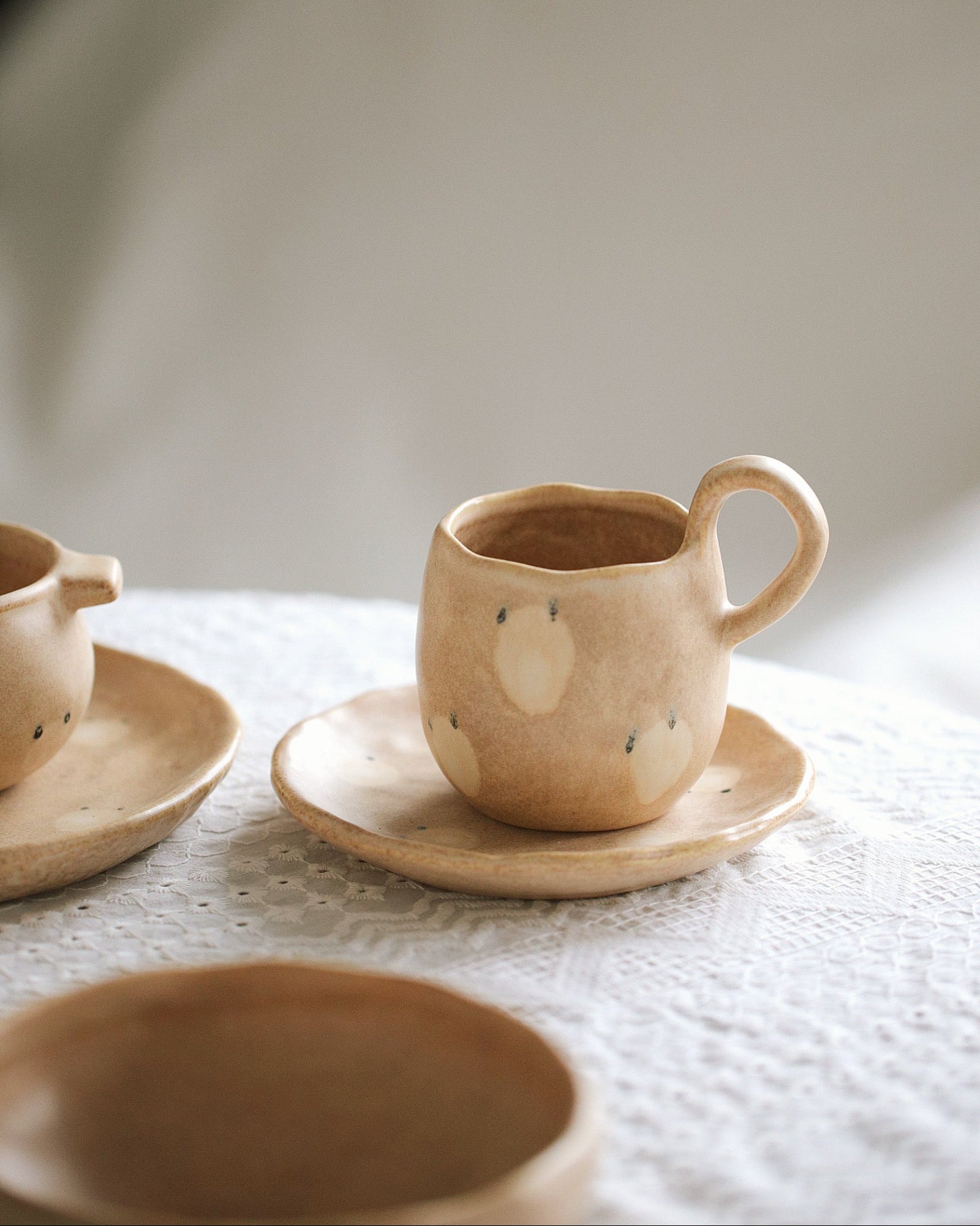 Set of ceramic dishes with a cup, saucer, and bowl on a textured surface.
