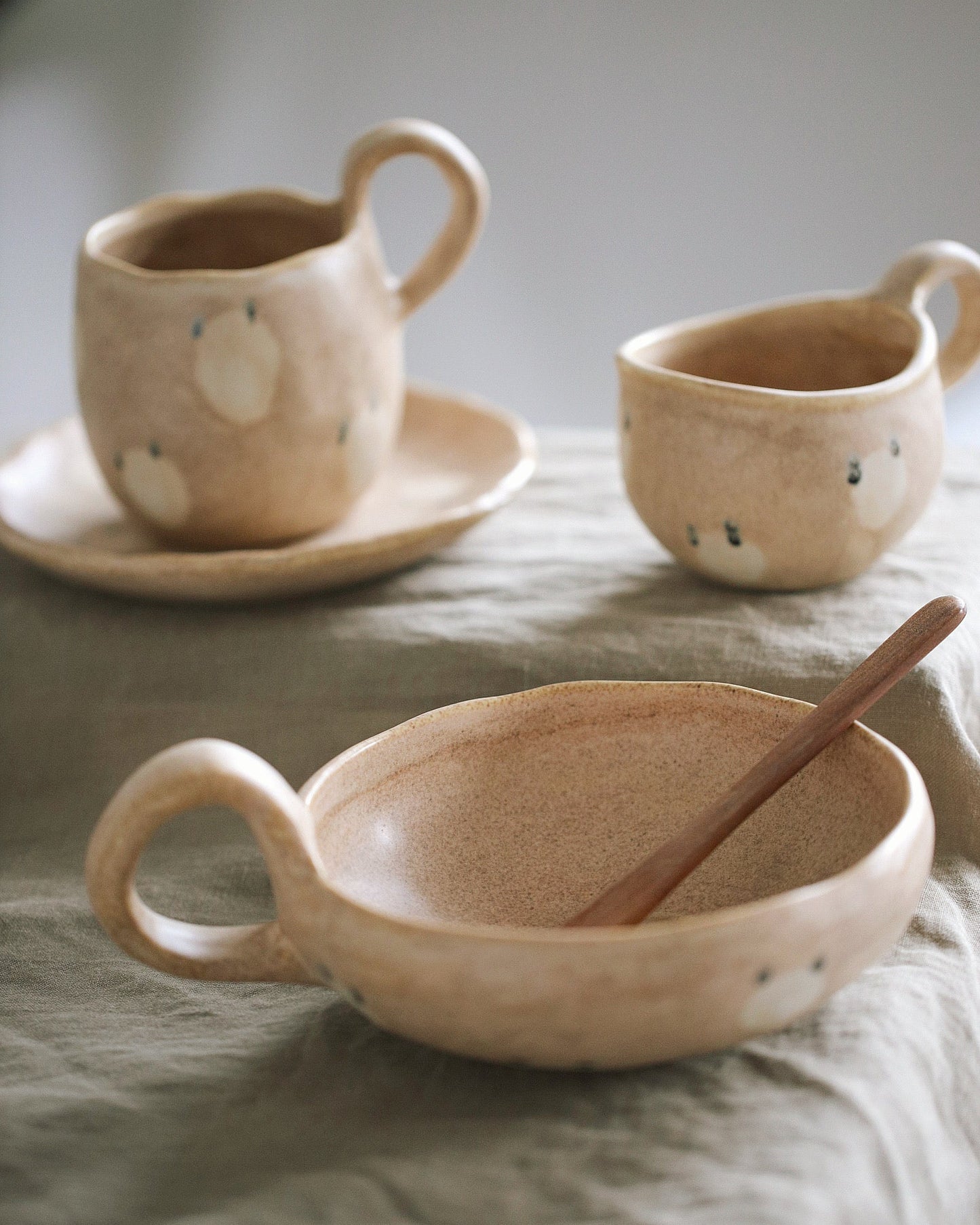 Set of ceramic dishes including a bowl, cup, and saucer on a textured surface.