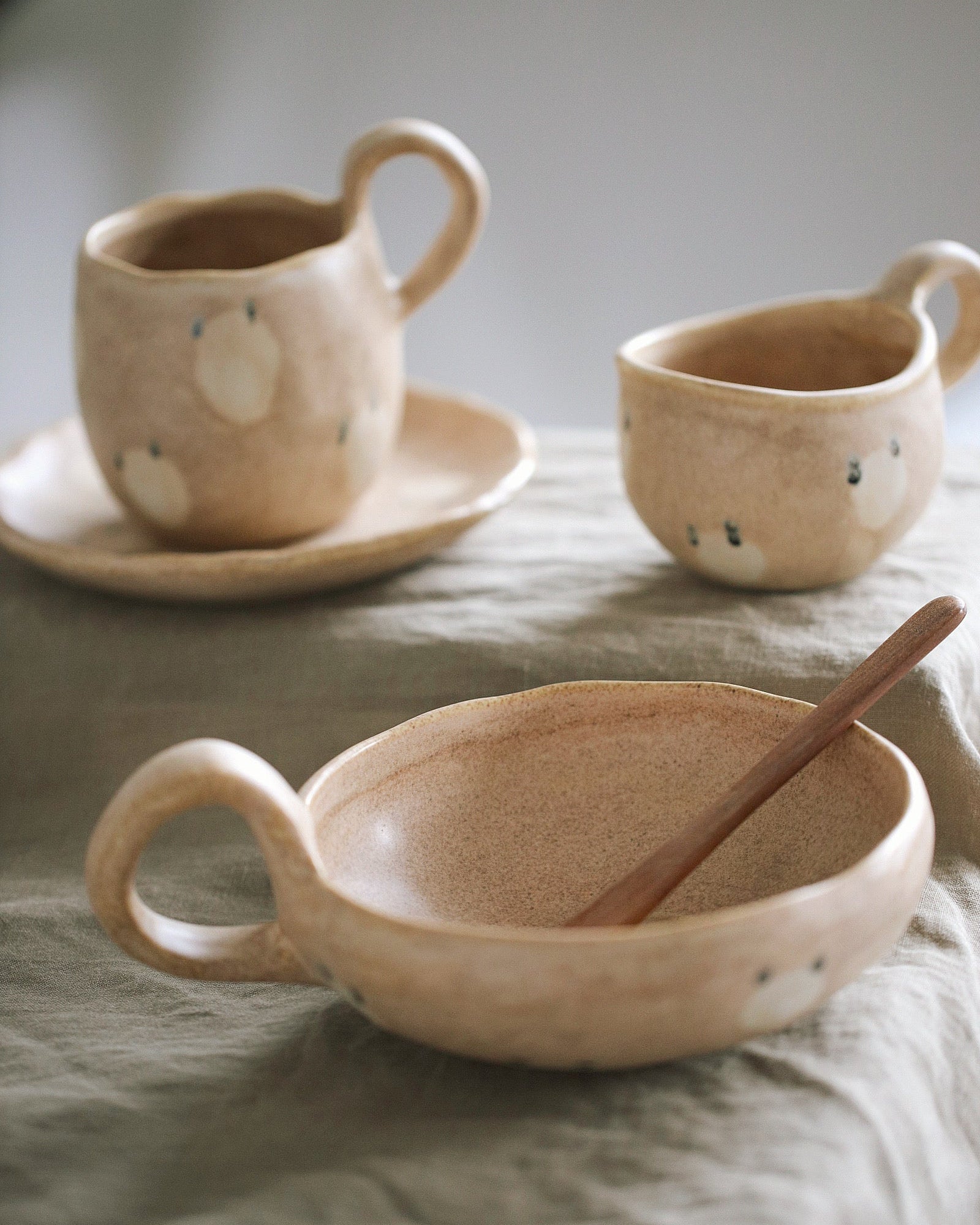 Set of ceramic dishes including a bowl, cup, and saucer on a textured surface.