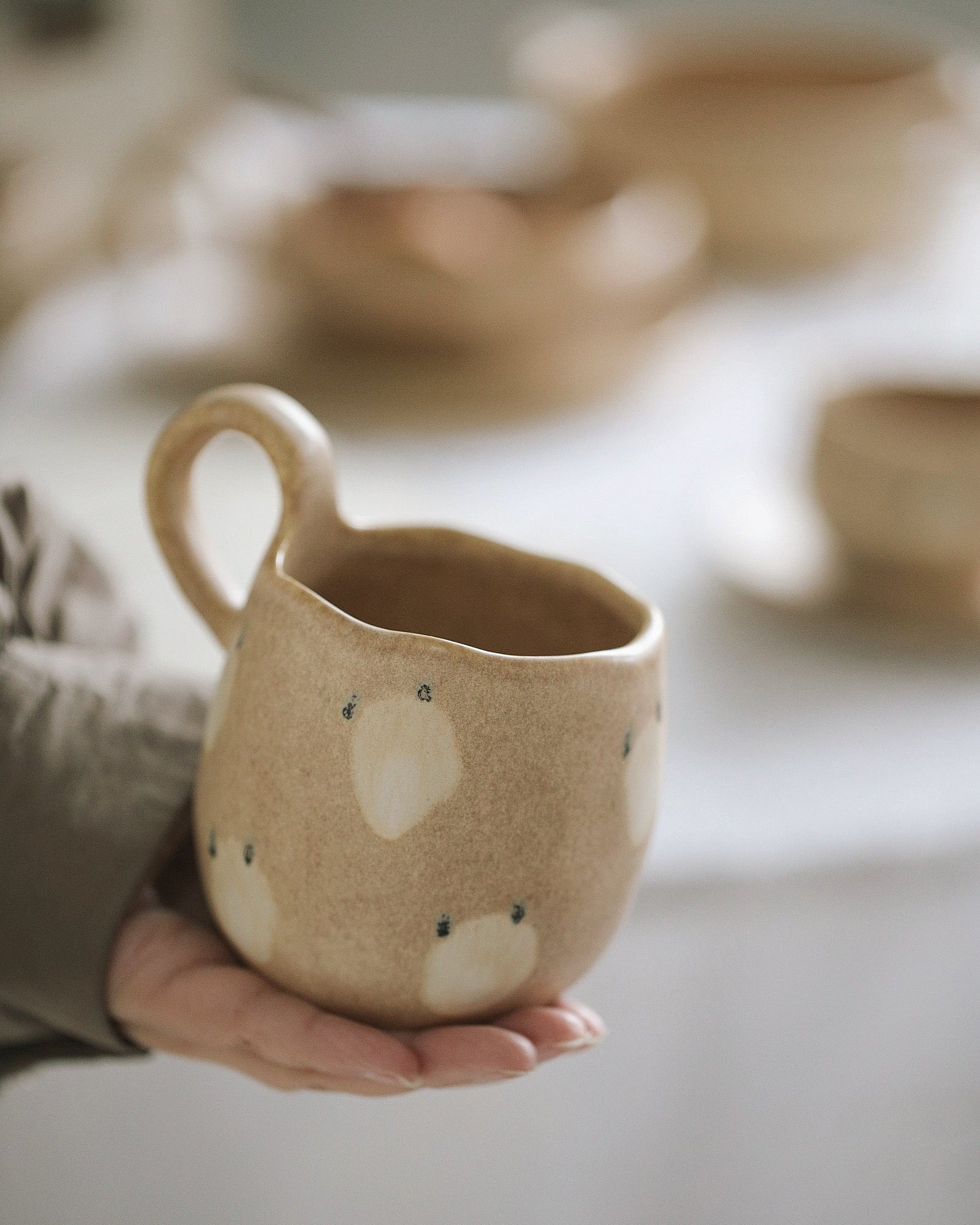 Hand holding a ceramic mug with a bear design in a blurred indoor setting