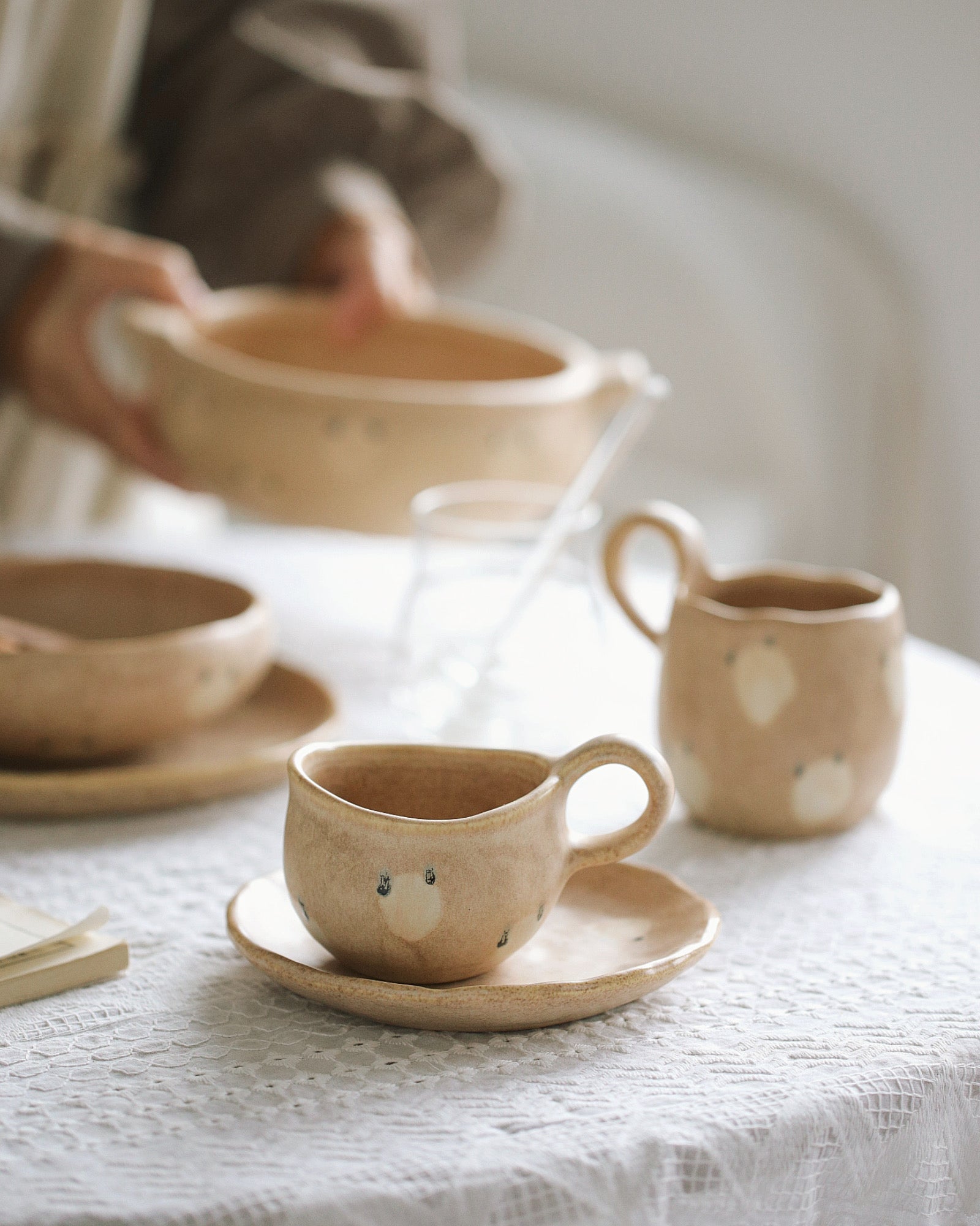 Ceramic tea set with teapot, cups, and saucers on a white tablecloth.