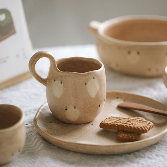 Ceramic mug with white polka dots on a matching plate with cookies and a wooden spoon, set on a textured surface.