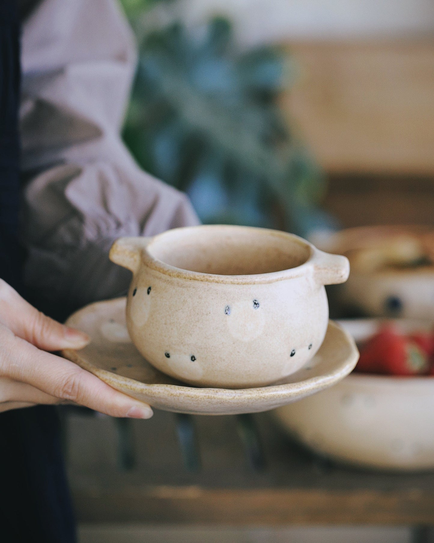 Person holding a small ceramic pot on a saucer with a blurred background