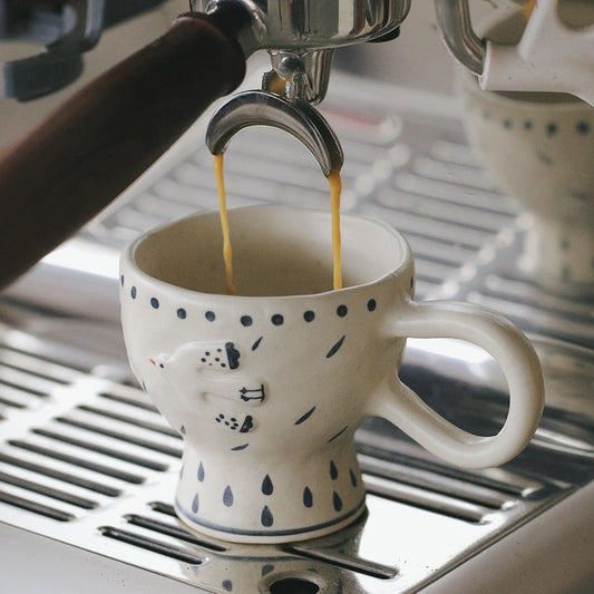 Espresso being poured into a white mug with black patterns on a silver espresso machine.