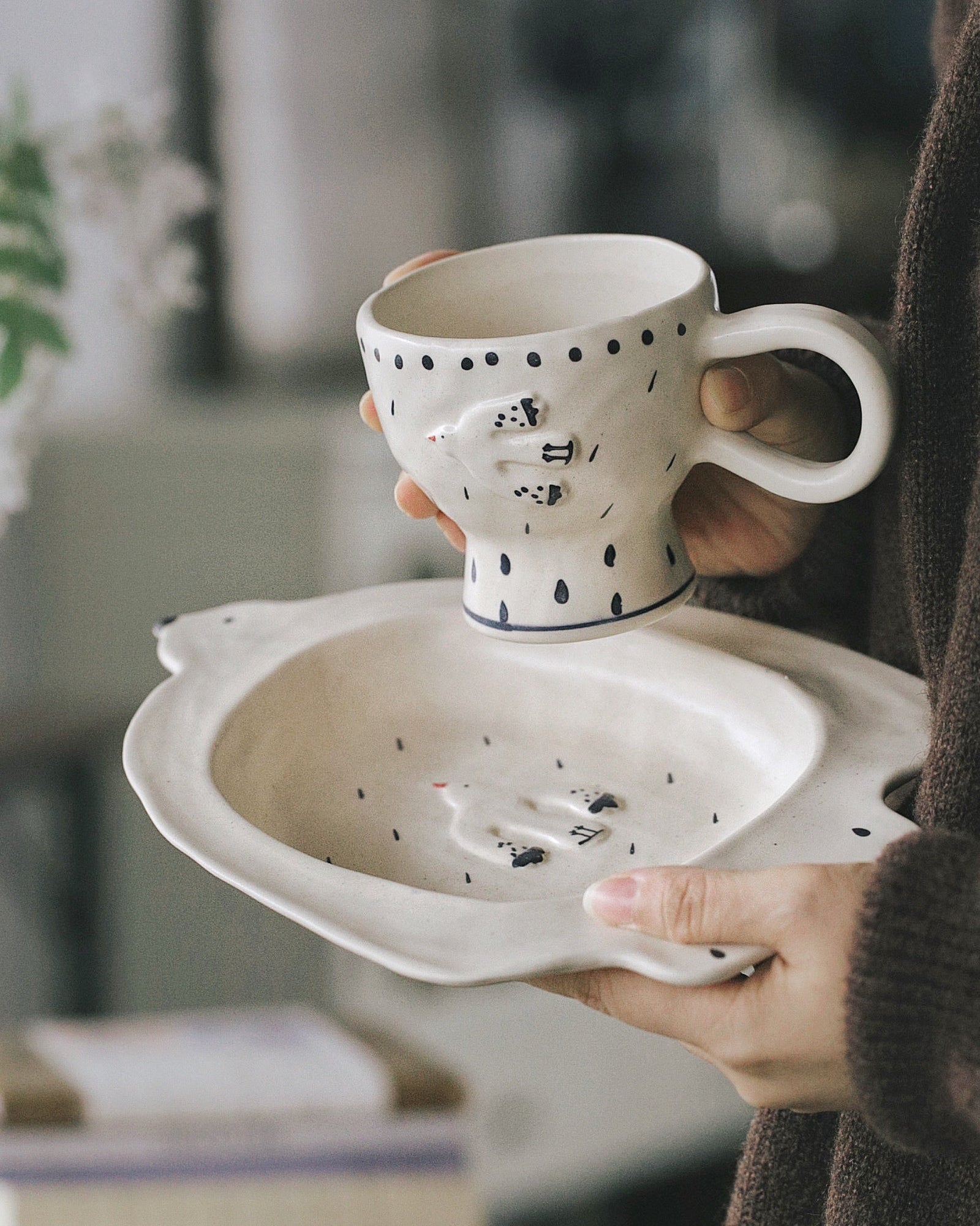 Person holding a ceramic cup with a decorative design on a blurred indoor background