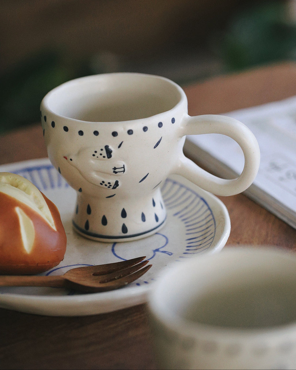 Ceramic mug with polka dot design on a wooden table with a pastry and book in the background