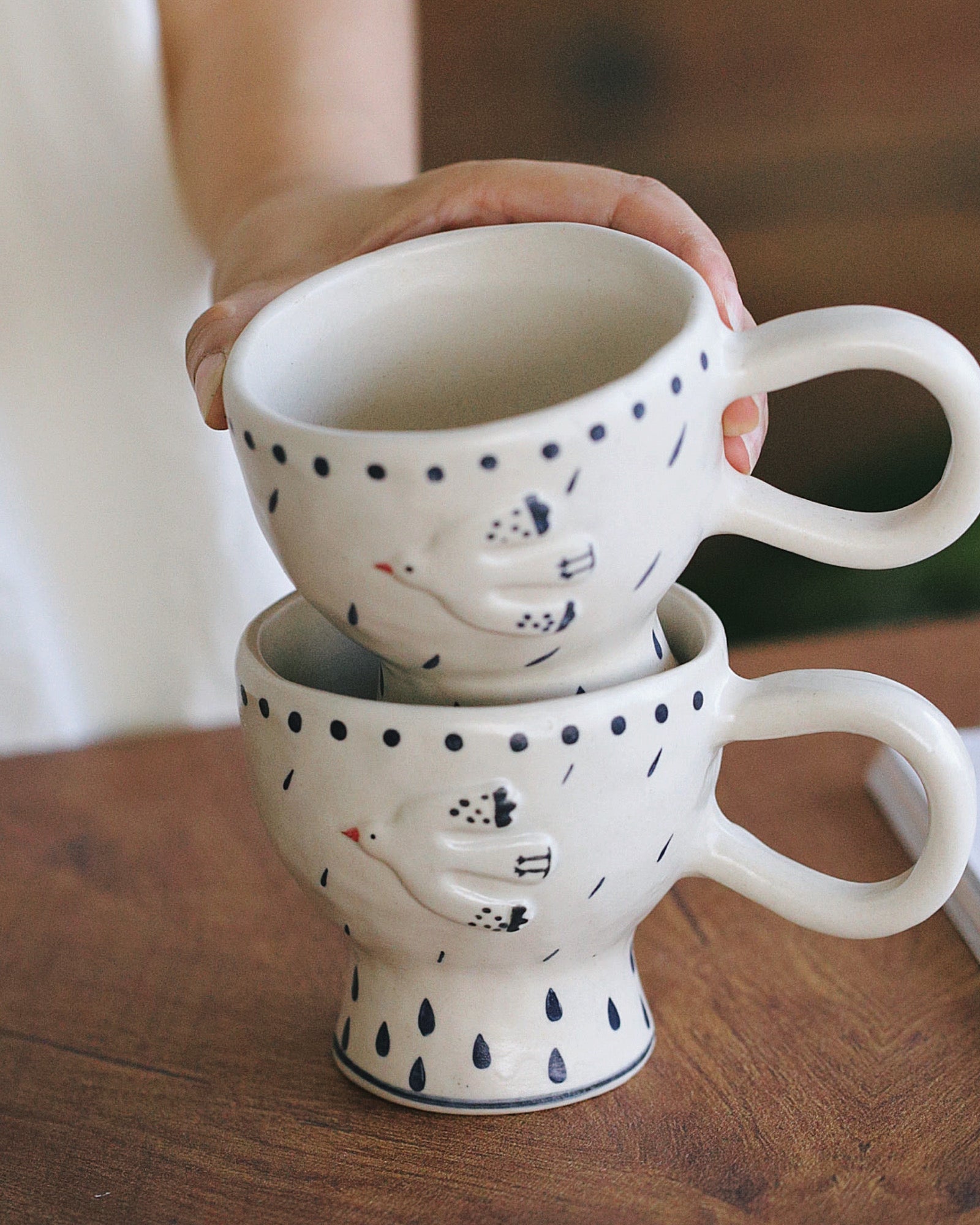 Two stacked ceramic mugs with polka dot patterns on a wooden surface.