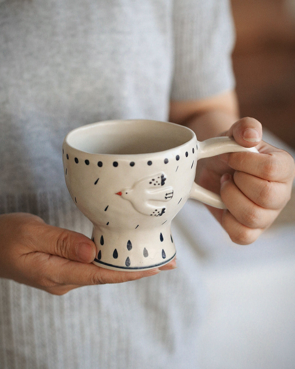 Person holding a ceramic mug with a bird design