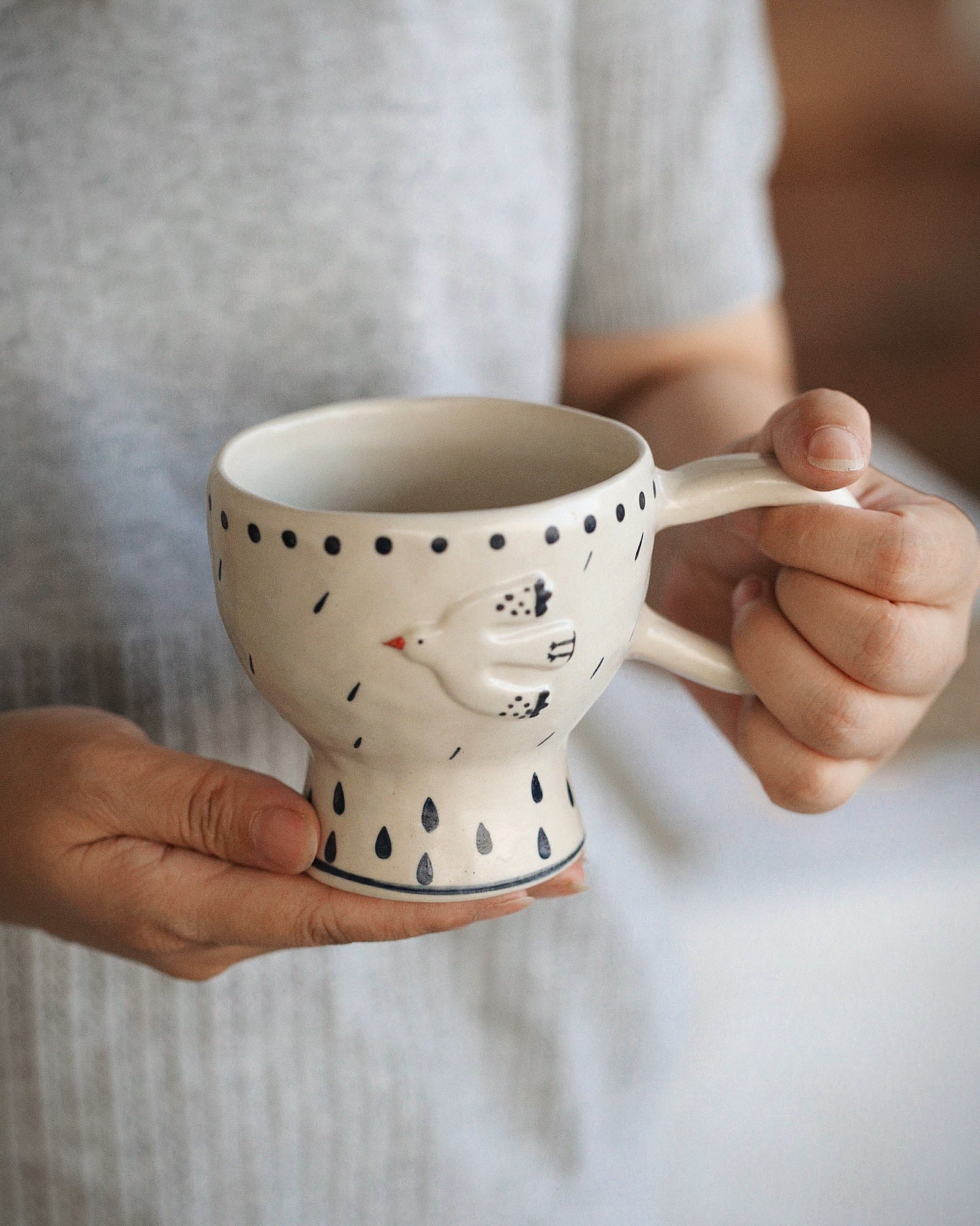 Person holding a ceramic mug with a bird design