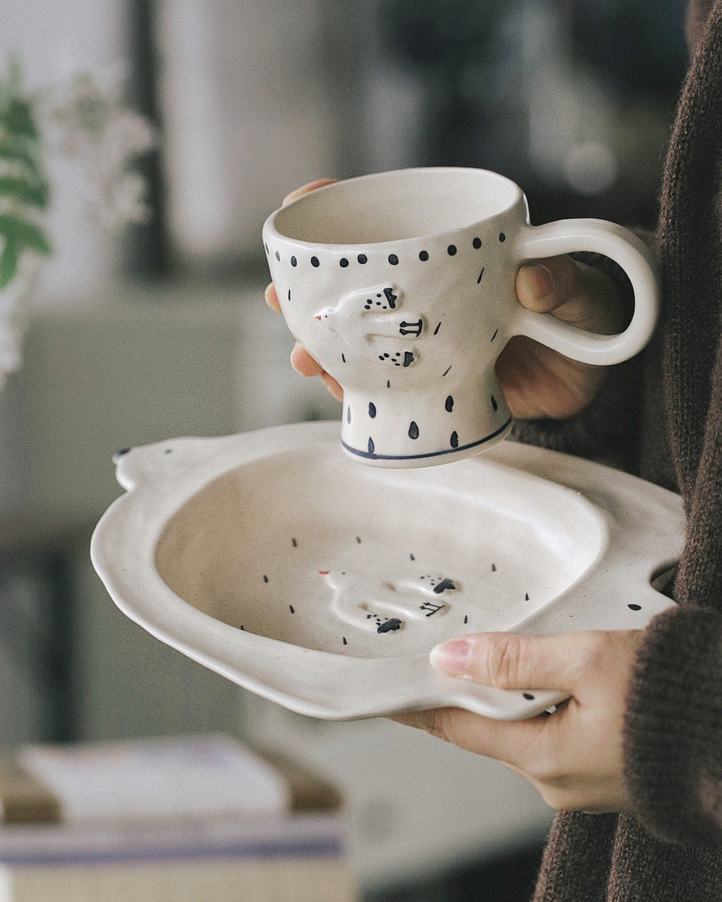 Person holding a ceramic cup with a decorative design on a blurred indoor background