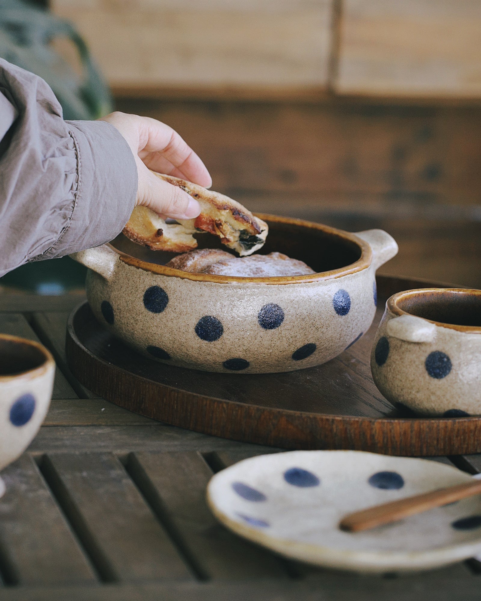 Person dipping food into a polka dot ceramic bowl on a wooden table