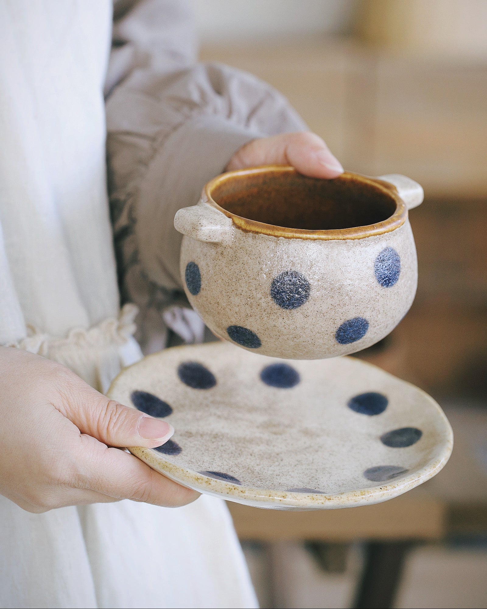 Person holding a ceramic pot with blue polka dots and matching plate.