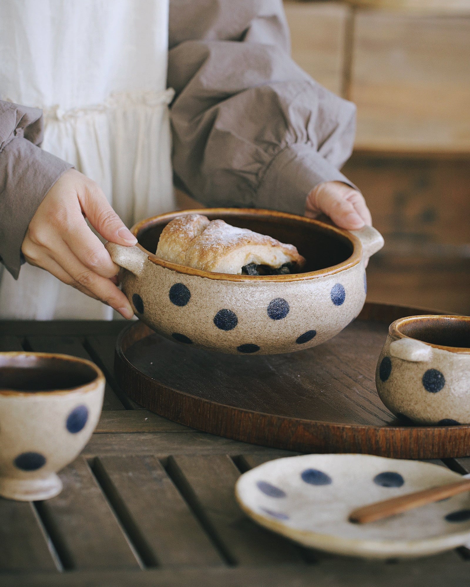 Person holding a ceramic bowl with polka dot pattern on a wooden table.