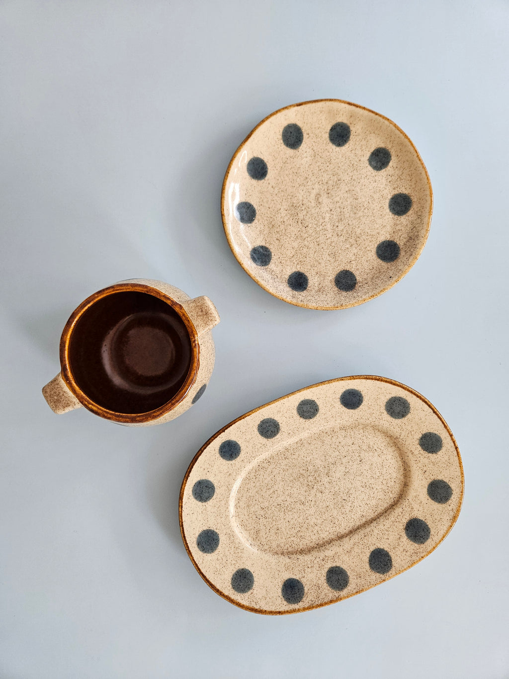 Set of ceramic plates and a mug with black dot patterns on a light gray background