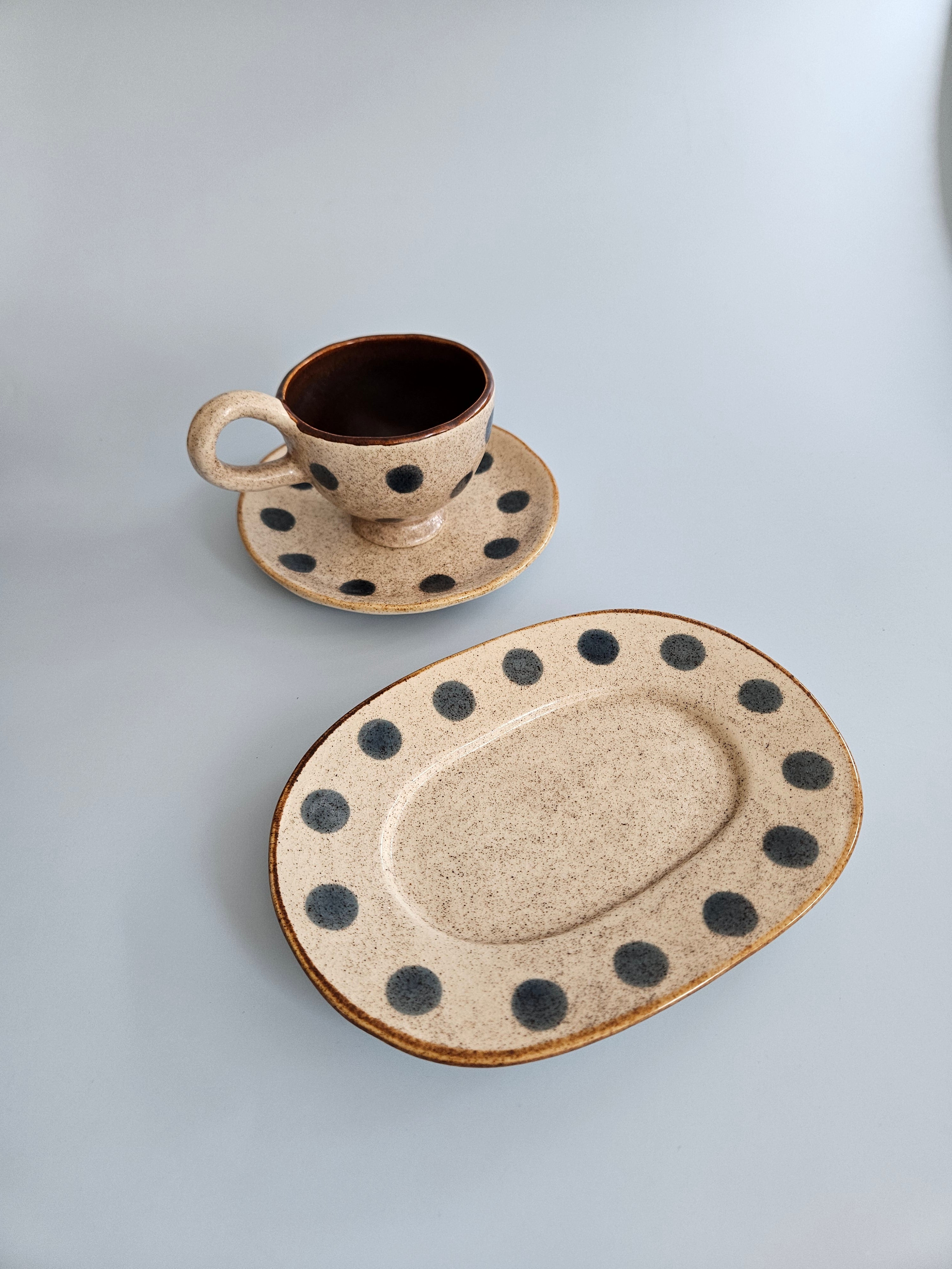 Ceramic cup and saucer with black speckles on a light gray background