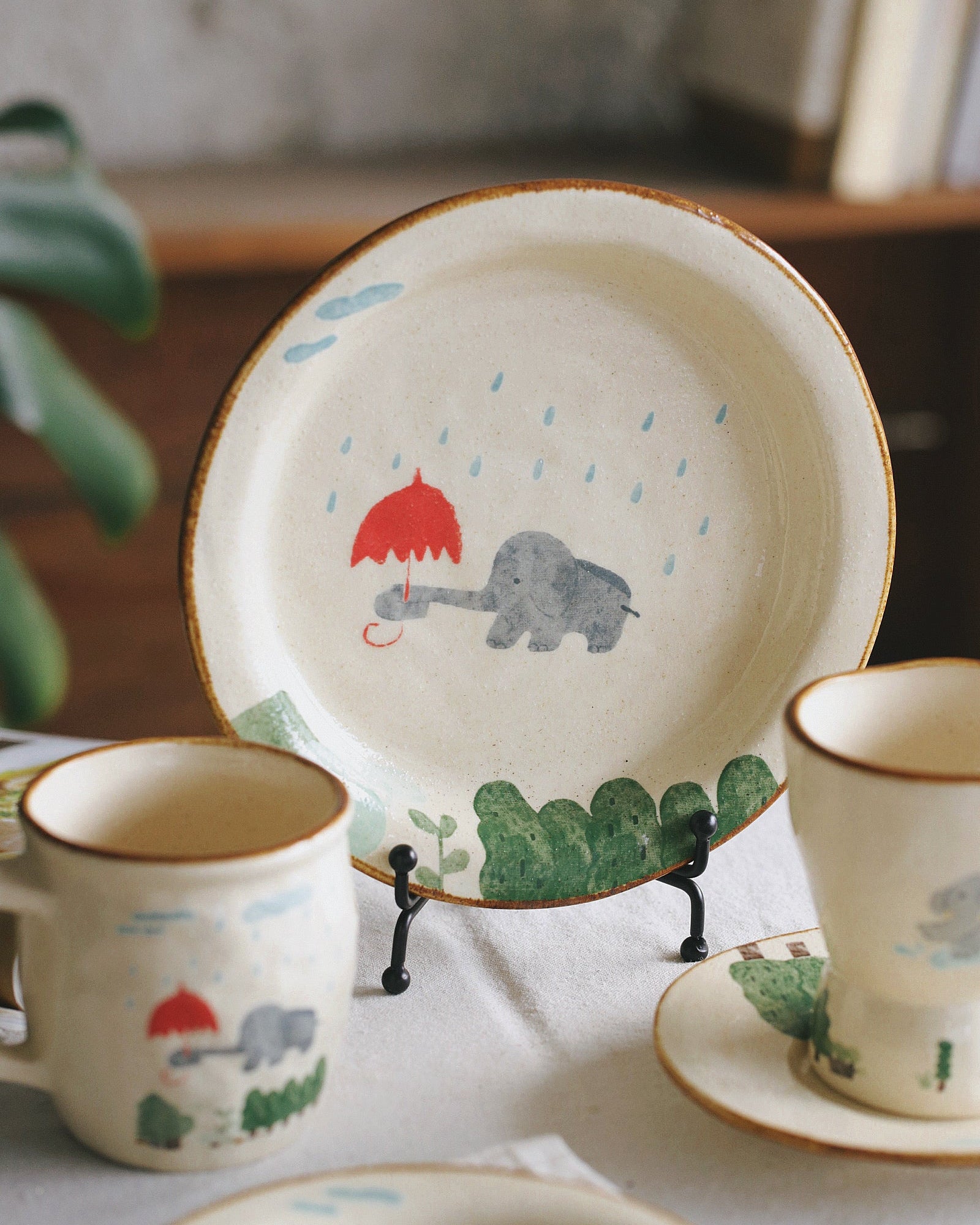 Children's ceramic set with elephant and umbrella design on a white surface.