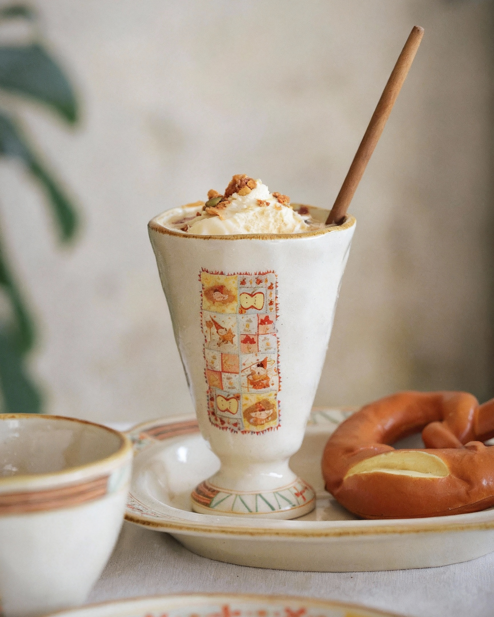Decorative cup with whipped cream and a cinnamon stick, surrounded by pastries on a light background