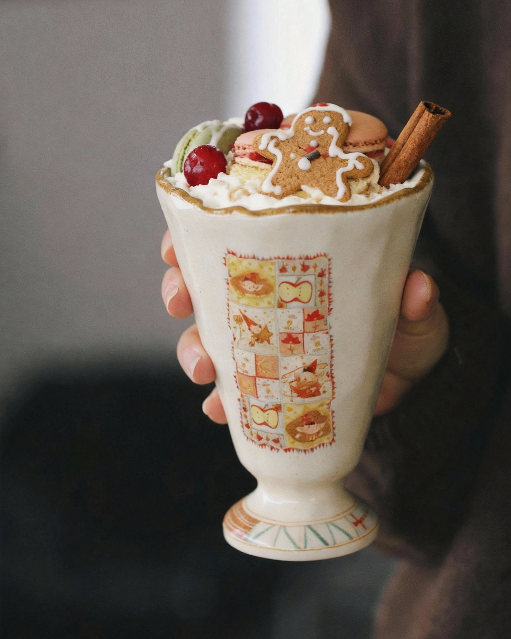 Decorative cup with hot chocolate and toppings held by a person