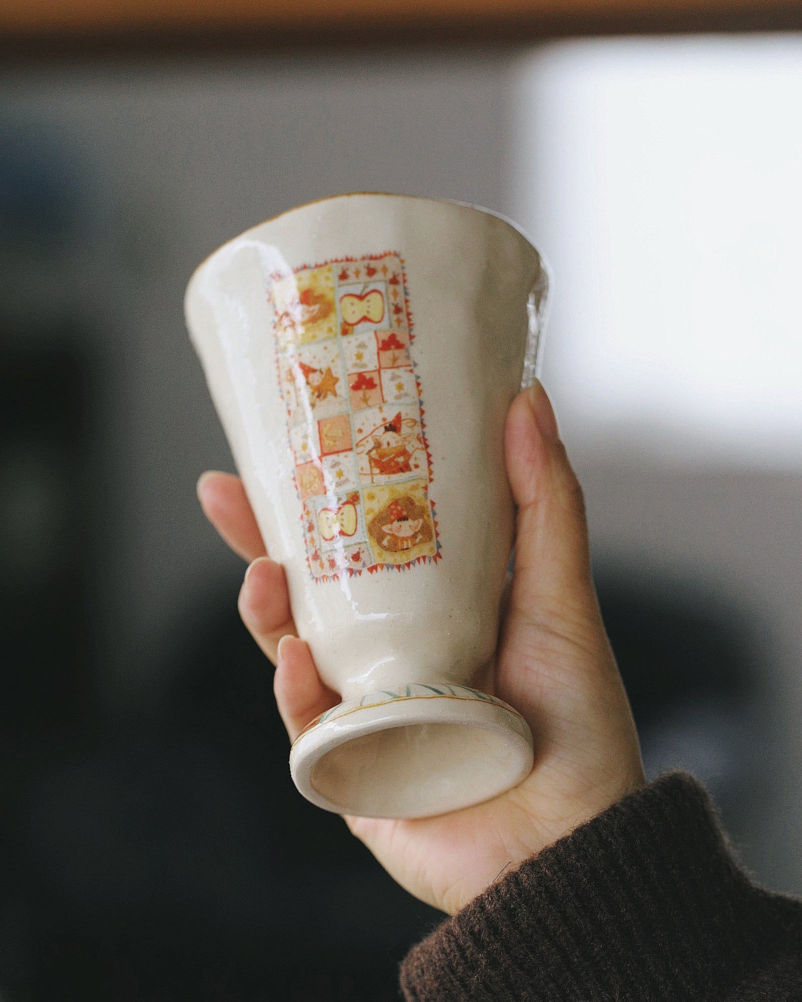 Hand holding a ceramic cup with decorative patterns against a blurred background
