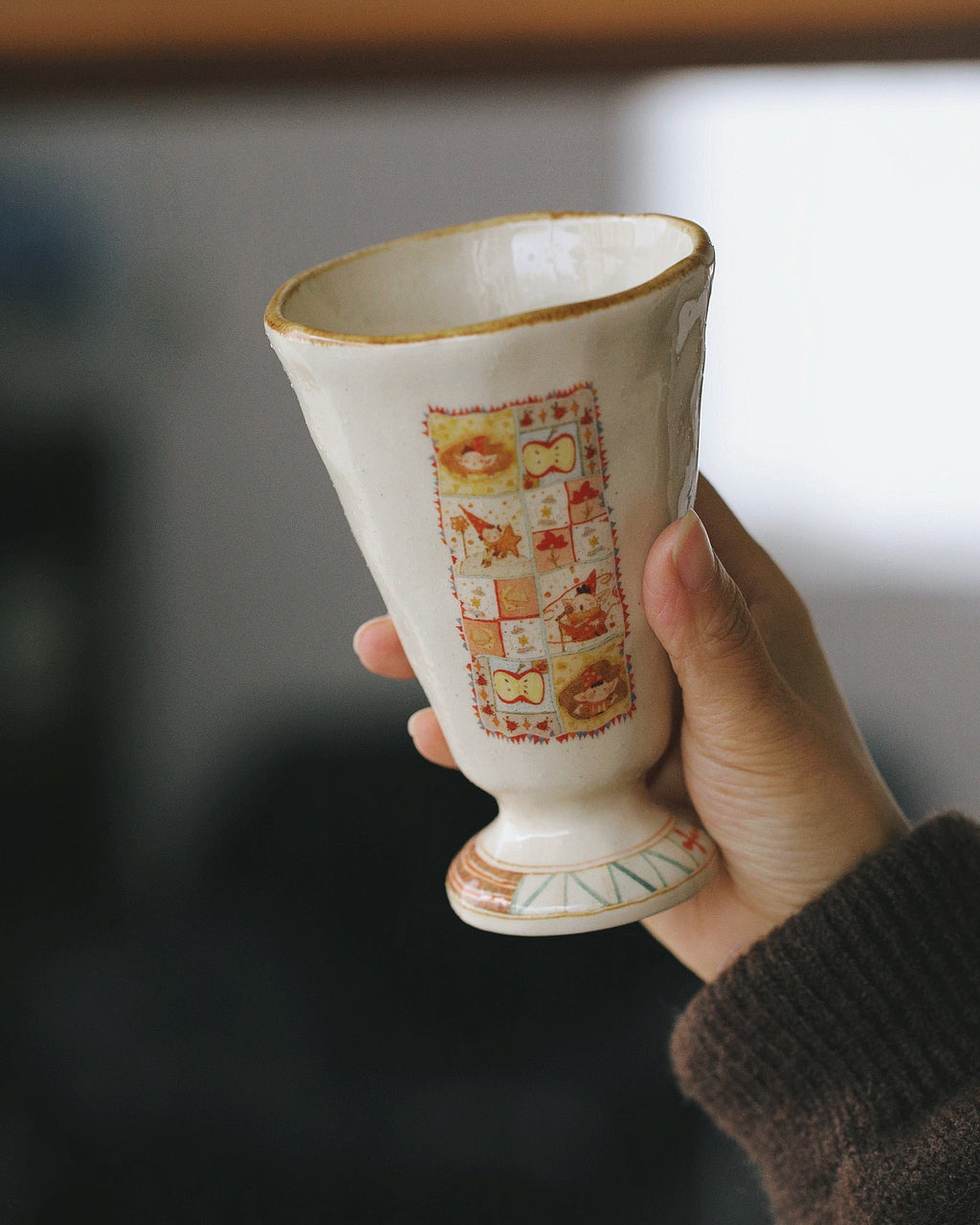 Ceramic cup with decorative pattern held by a hand against a blurred background