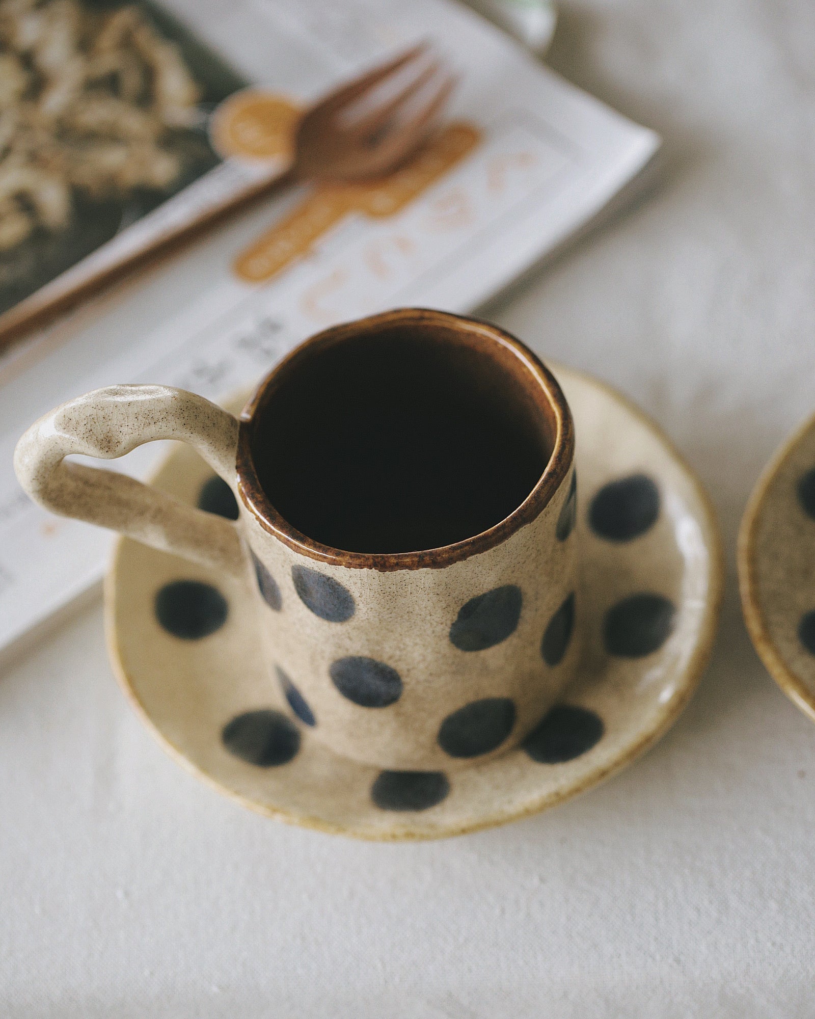 Ceramic cup with polka dot design on a saucer, filled with dark liquid, on a white surface.