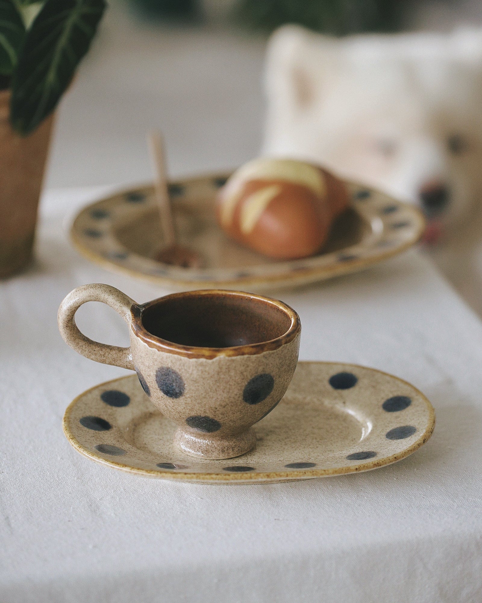 Ceramic cup with polka dots on a matching saucer, placed on a white surface with a blurred background.
