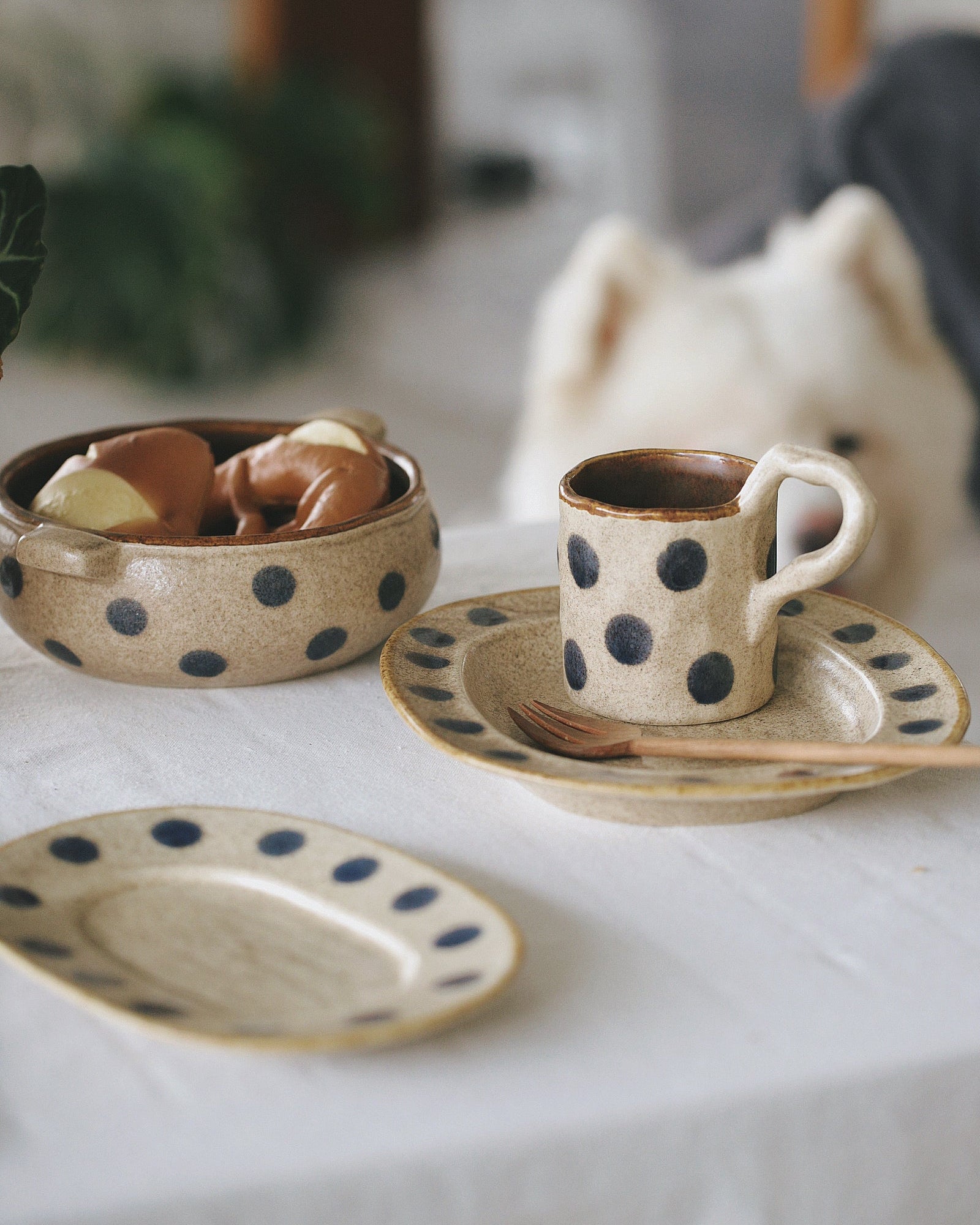 Ceramic polka dot cup and saucer with a bowl of food on a white tablecloth.