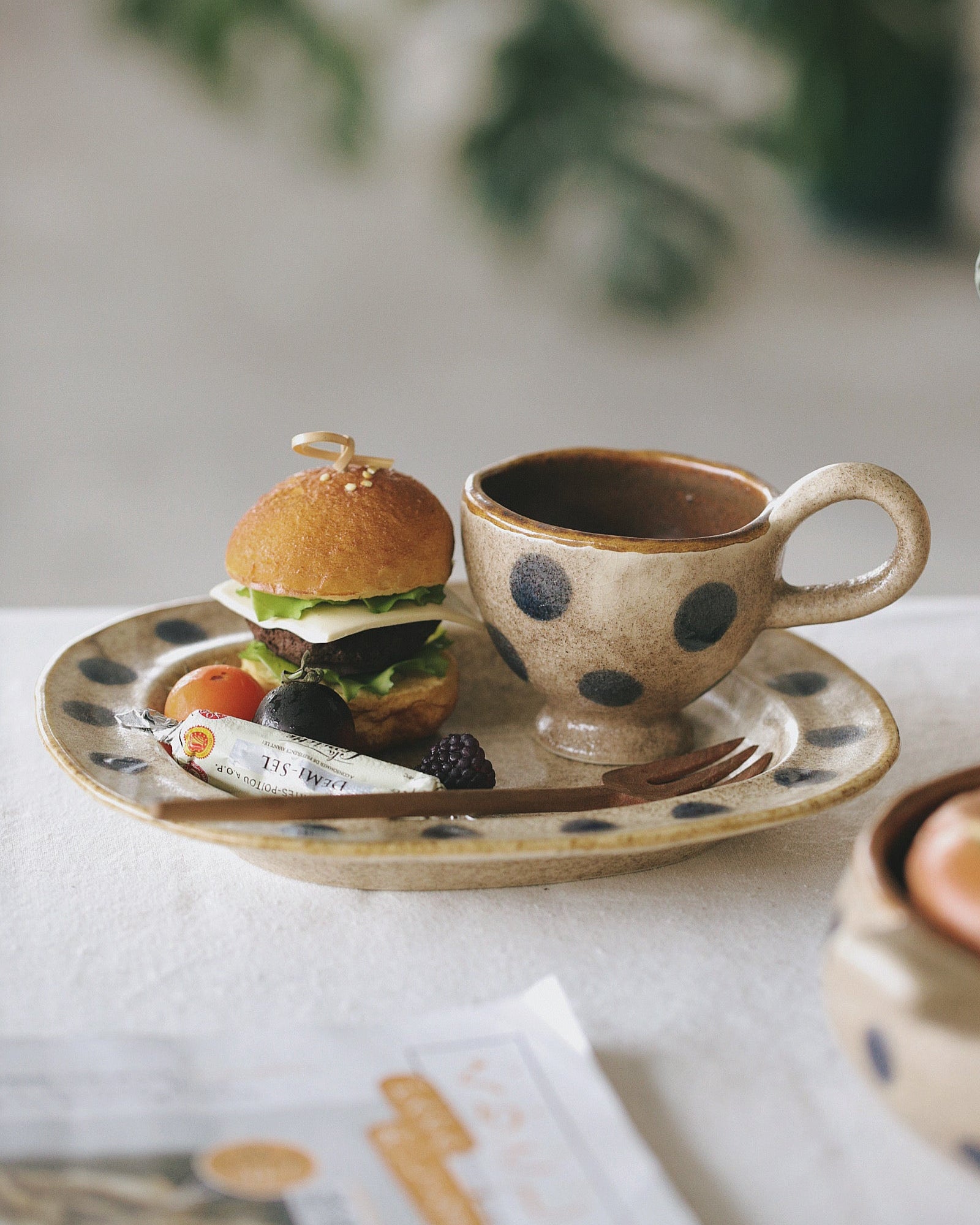 Small burger and polka dot cup on a plate with a blurred green plant in the background