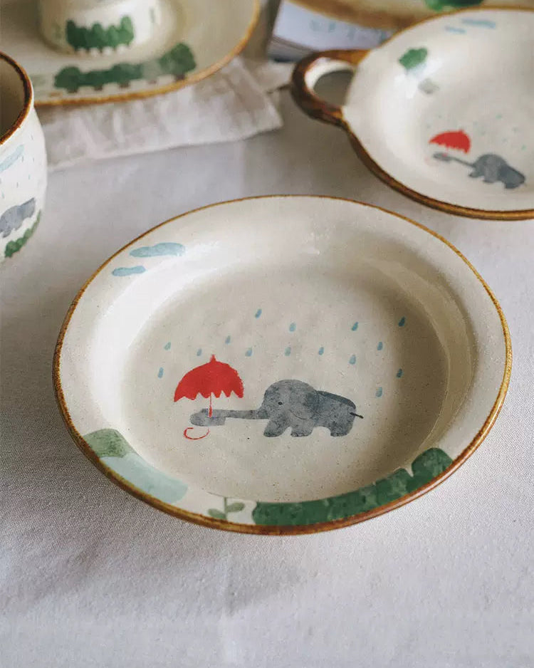 Children's ceramic plate with an elephant holding a red umbrella design on a white tablecloth.